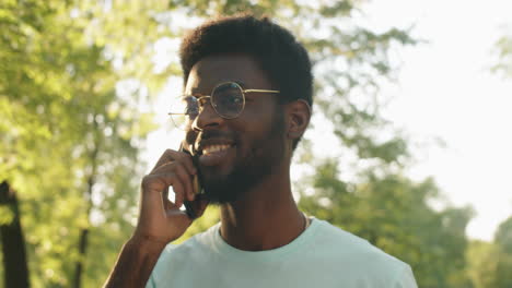 Junger-Afroamerikanischer-Mann,-Der-Im-Park-Spaziert-Und-Telefoniert